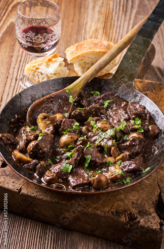 Traditional French venison ragout witch mushroom in Burgundy red wine sauce served as close-up in a rustic wrought-iron pan