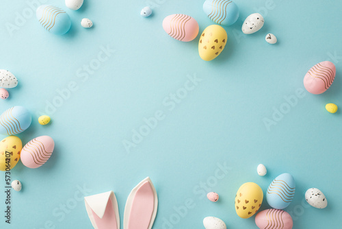 Easter party concept. Top view photo of easter bunny ears white pink blue and yellow eggs on isolated pastel blue background with copyspace in the middle