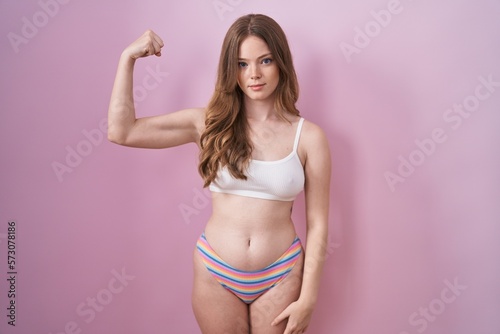 Caucasian woman wearing lingerie over pink background strong person showing arm muscle, confident and proud of power