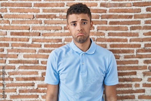 Brazilian young man standing over brick wall depressed and worry for distress, crying angry and afraid. sad expression.