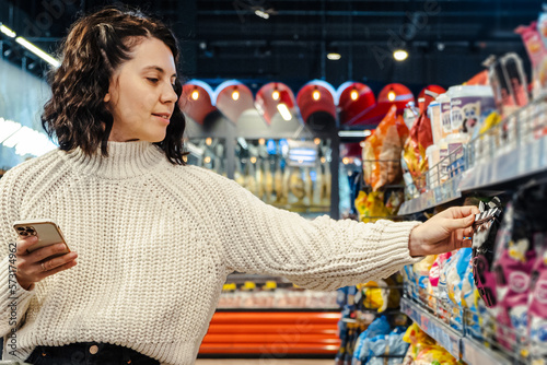 a woman chooses a product from a list of products on the phone in a supermarket