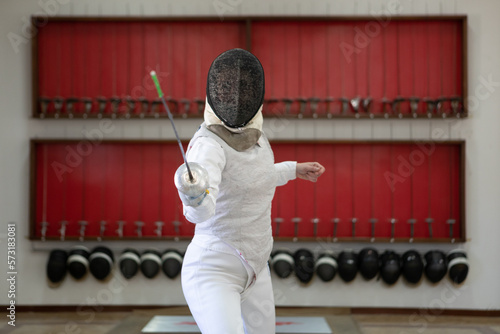 Una mujer armada con un florete practica esgrima en instalaciones deportivas.