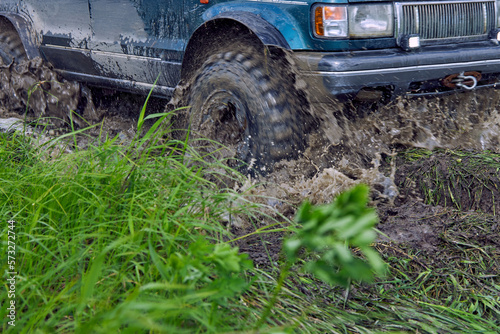 The blue SUV is driving on a bad road, interfering with mud and slush with the wheels. Offroader participates in an off-road race.