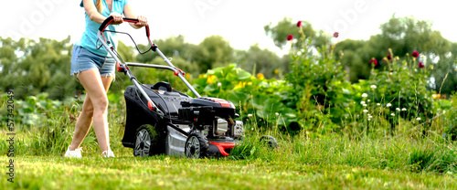 a girl mows the lawn with a lawn mower