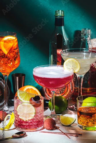 Alcoholic cocktails drinks set, strong alcohol bottles, liquor and bitters, bar tools, dark green interior background, trendy hard light. Martini vodka, pink lady, aperol spritz, margarita