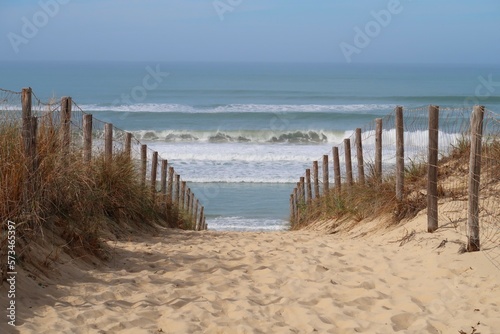 Chemin de sable cloturé par une ganivelle et descendant vers la mer et la plage des Dunes à Lège Cap Ferret, en Gironde, avec vue sur les vagues déferlantes de l'océan Atlantique (France)