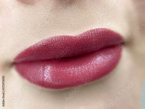 permanent makeup on the lips of a young woman of a delicate peach shade close-up, a girl after a cosmetic procedure with smooth and clean healthy skin.