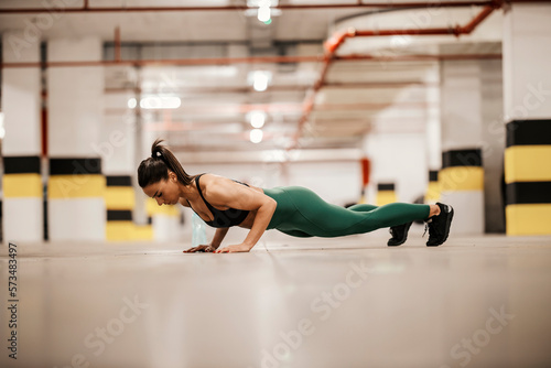 An urban muscular sportswoman is doing pushups in underground garage.