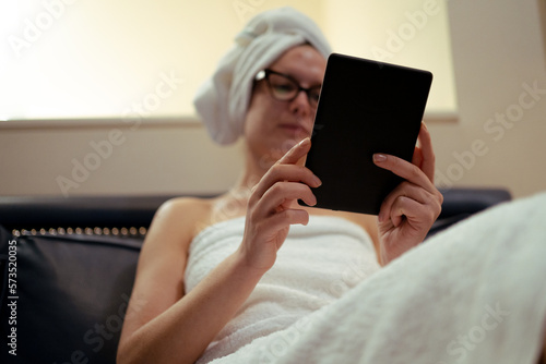 Young girl with eyeglasses reading an ebook relaxed after showering, beauty routine, at home