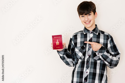 Young teenager boy holding Mongolia passport looking positive and happy standing and smiling with a confident smile against white background.