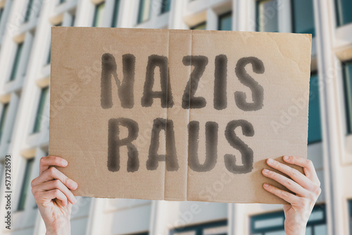 The phrase " Nazis out " is on a banner in men's hands with blurred background. Estrangement. Hostility. Discord. Contention. Strife. Controversy. Polemic. Altercation. Dispute. Wrangle. Quarrel