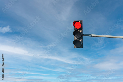 Modern traffic light with red light in front of cloudless sunny blue sky
