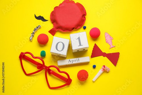 Composition with date 1 APRIL and party decor on yellow background. April Fool's Day celebration