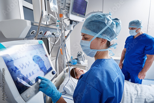 Hospital nurses checking on woman patient at intensive care unit and monitoring her health with medical equipment and sensors. ICU