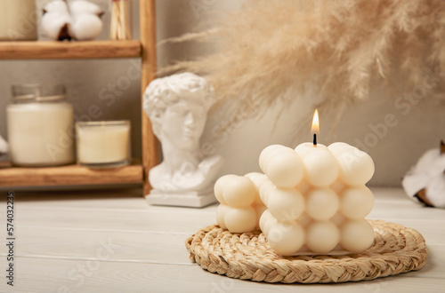 Soy wax candle on a textured table. Interior decor with a handmade burning candle. Hygge home decoration concept and aromatherapy. Bubble candle on the background of a textured wall.