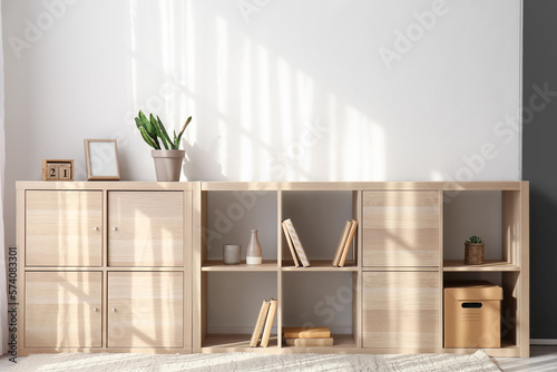 Wooden chest of drawers with books and decor near light wall