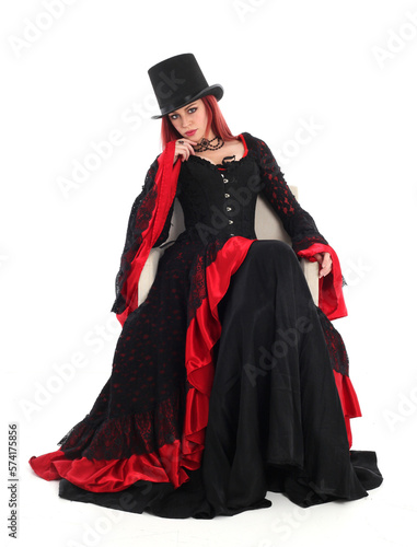portrait of beautiful red haired woman wearing long black fantasy vampire costume gown, isolated pose on studio background.