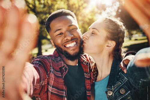 Interracial couple, selfie kiss and portrait in nature, having fun and bonding together outdoors. Smile, love romance and black man and woman kissing to take photo for happy memory or social media.