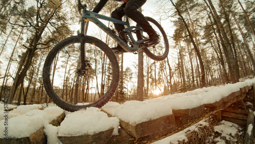 CLOSE UP: Bike rider doing wheelie in beautiful golden light on snowy trail