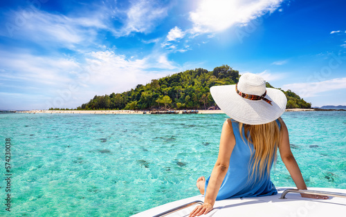 A beautiful tourist woman with sunhat sits on a yacht and looks at the turquoise sea and beaches of Bamboo island in the Krabi region, Thailand