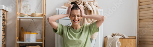 tensed woman touching head near washing machine in laundry room, banner.