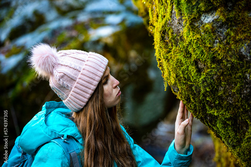 Beautiful girl in blue jacket touch and observe green moss covered rock in Yosemite National Park, California, USA. Bond with nature motive.