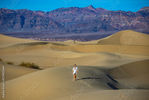 beautiful girl in lace dress lost in the middle of sandy desert; walking through mesquite flat sand dunes at sunset