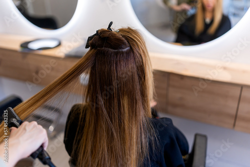 From above back view of unrecognizable female client sitting near mirror in beauty salon during keratin hair straightening procedure