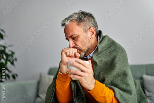 Allergic sick senior man coughing with a sore throat, holding a cup of tea.