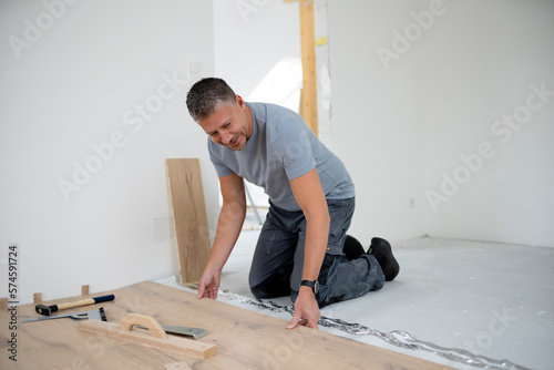 Middle aged man with grey hair and grey shirt laying parquet floor in new loft, house