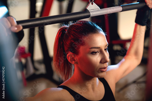Portrait of a 30s woman working out on a lat machine in a gym.