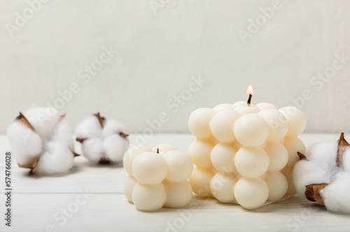 Bubble candle on a textured wooden table. Trendy soy candle. Eco product. Interior decor with handmade burning candle. Side view. Close-up. Place for text.
