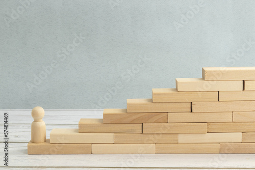 wooden figurine of a man stands on a staircase made of blocks on the first step.