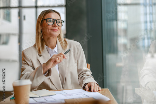 Businesswoman architect in glasses working on project while sitting in cafe and looking at window