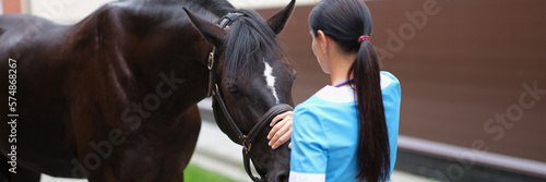 Veterinarian strokes and communicates with horse outdoors