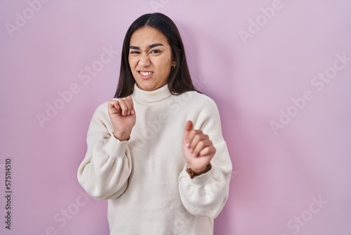 Young south asian woman standing over pink background disgusted expression, displeased and fearful doing disgust face because aversion reaction.