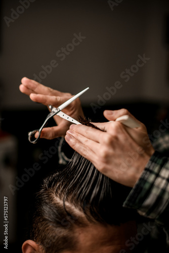 close-up view on hands of barber holding strand of hair and scissors and do haircut