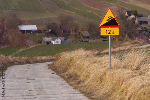 Znak ostrzegawczy o nachyleniu drogi 12% na wiejskiej drodze. 