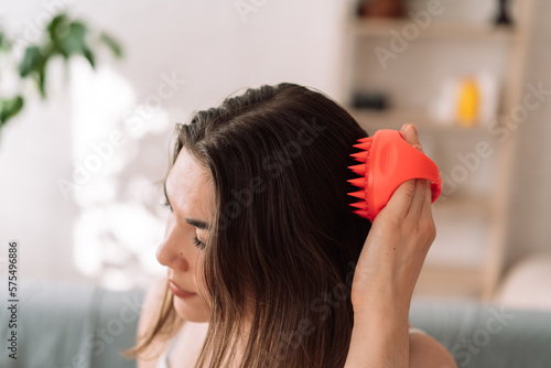 Girl enjoys doing herself a head massage using a scalp massager.