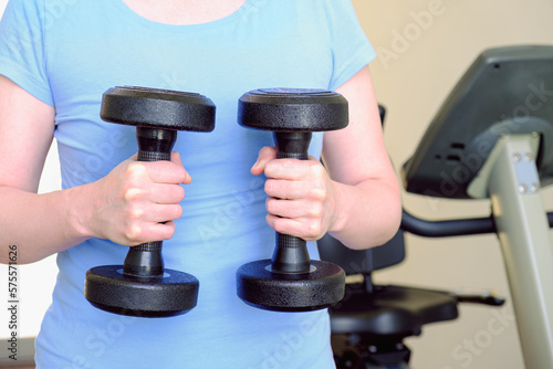 Woman in the gym holds a metal dumbbells. Sports equipment for increasing muscle mass. The concept of doing sports, healthy lifestyle