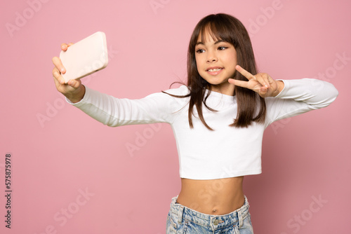 Photo of charming cute schoolgirl dressed t-shirt tacking selfie modern device showing v-sign isolated pink color background