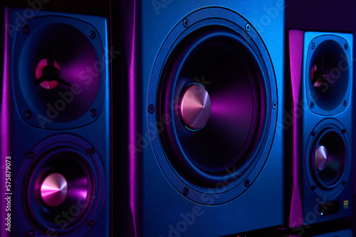 Two sound speakers and subwoofer on dark background with neon lights. Set for listening music. Audio equipment