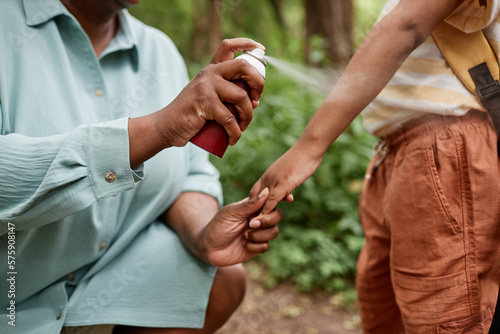 Closeup of caring black mother using baby safe bug repellent for daughter while hiking together 