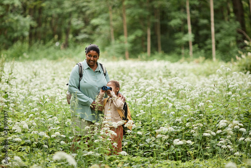 Portrait of black mother and daughter hiking in nature and looking in binoculars, copy space 