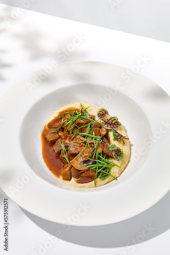 Elegant stew beef with mashed potatoes in restaurant. Beef bourguignon on light background with shadows of leaves Braised black angus meat with potato cream in summer menu