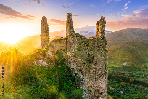 immersive landscape of old castle ruins on foreground and beautiful mountains with sunset with clouds on background