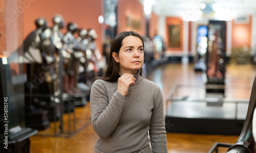 Female museum visitor examining with interest ancient iron armor displayed on exhibition ..