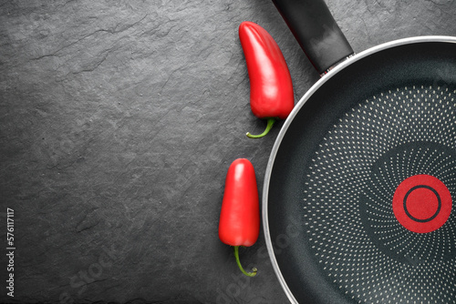 Blank skillet with non-stick coated surface on the black slate with red peppers. Copy space.