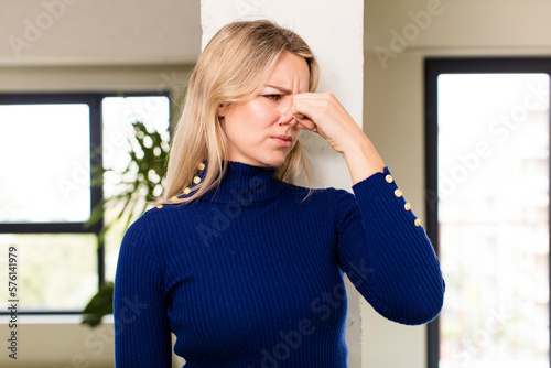 young pretty woman feeling disgusted, holding nose to avoid smelling a foul and unpleasant stench