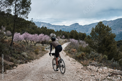 Fit male cyclist is riding dirt trails on a gravel bike. A man riding a gravel bike on a gravel road in a scenic view with hills in Castell de Castells,Alicante region, Spain. 